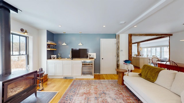 living area with light wood finished floors, wine cooler, beam ceiling, and a wood stove