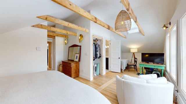 bedroom featuring baseboards, radiator, vaulted ceiling with beams, a spacious closet, and light wood-style floors