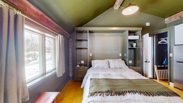 bedroom featuring light wood-style floors, freestanding refrigerator, and lofted ceiling with beams