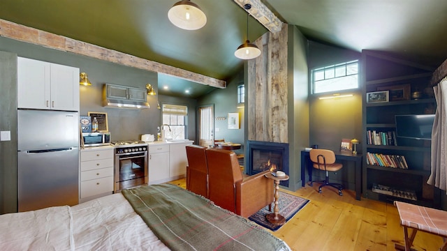 kitchen featuring stainless steel appliances, a large fireplace, white cabinetry, light wood-type flooring, and beamed ceiling