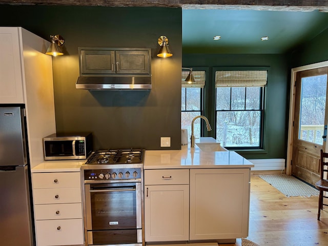 kitchen with range hood, stainless steel appliances, light countertops, light wood-type flooring, and a peninsula