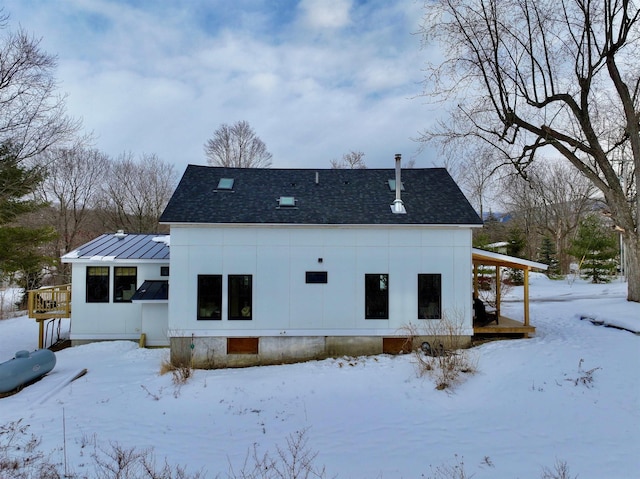 snow covered back of property featuring metal roof, a standing seam roof, and roof with shingles