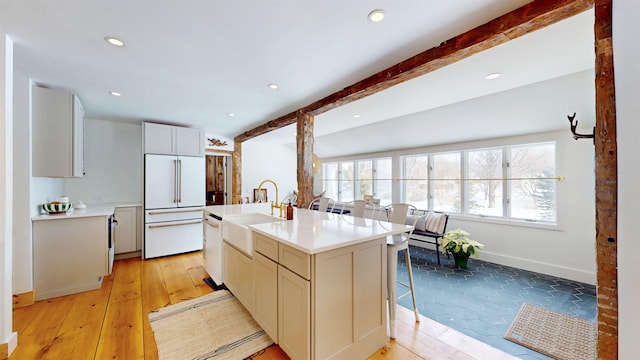 kitchen featuring high end fridge, light countertops, white dishwasher, a sink, and beamed ceiling