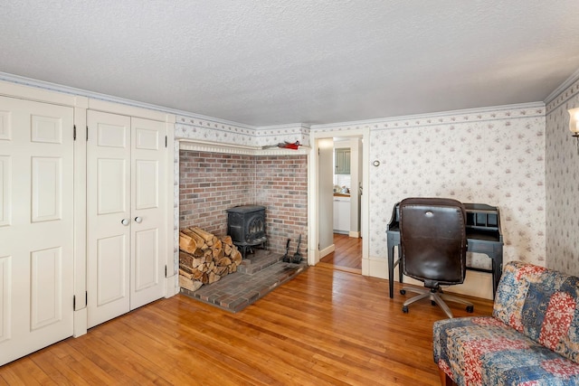 office space featuring crown molding, a wood stove, a textured ceiling, wood finished floors, and wallpapered walls