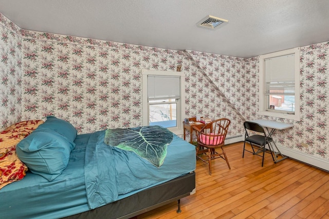 bedroom with wallpapered walls, baseboards, visible vents, hardwood / wood-style flooring, and a textured ceiling