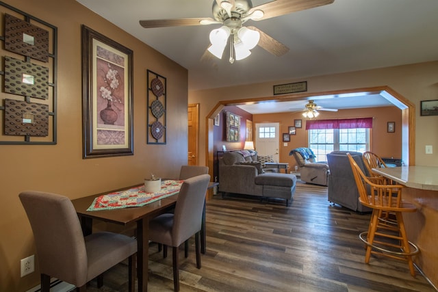 dining area featuring a ceiling fan, arched walkways, and dark wood-style flooring