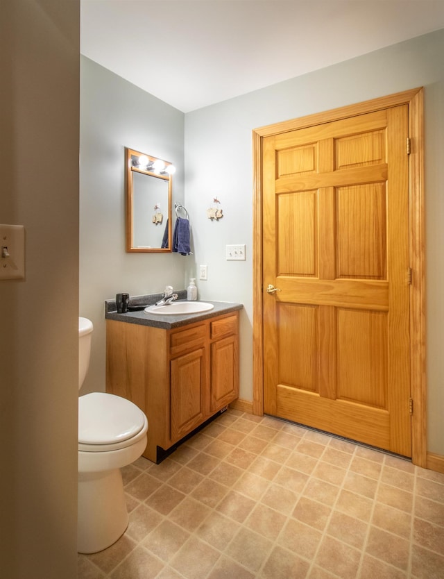 half bath featuring baseboards, vanity, and toilet