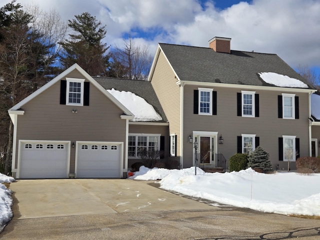 colonial home featuring driveway, a shingled roof, a garage, and a chimney