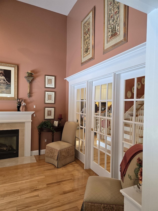 living area featuring light wood finished floors, a fireplace with flush hearth, a high ceiling, and baseboards