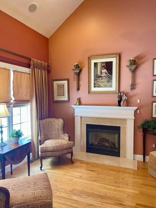 sitting room with baseboards, vaulted ceiling, wood finished floors, and a glass covered fireplace