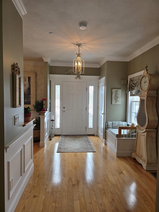 foyer entrance featuring ornamental molding, light wood finished floors, a chandelier, and a decorative wall