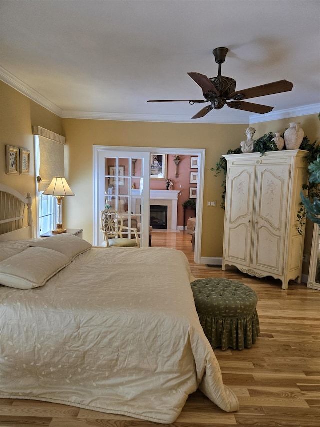 bedroom featuring ornamental molding, light wood-type flooring, a fireplace, and ceiling fan