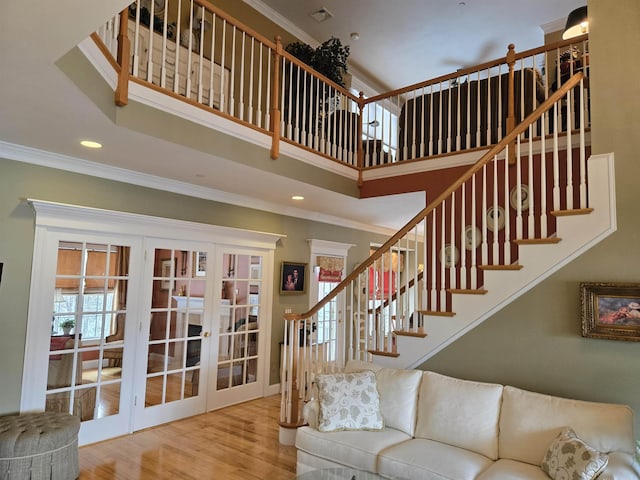 living area with a towering ceiling, stairway, ornamental molding, wood finished floors, and french doors