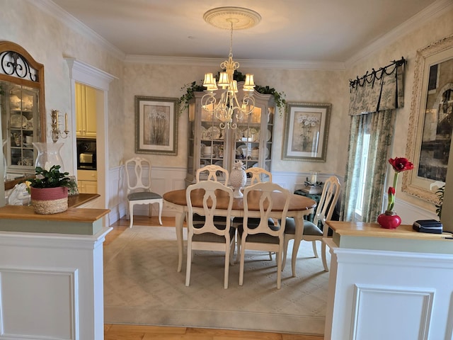 dining space featuring an inviting chandelier, ornamental molding, light wood-style floors, and wainscoting