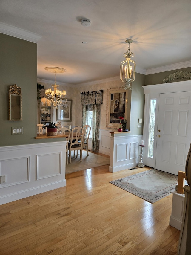 entryway with an inviting chandelier, ornamental molding, light wood finished floors, and a wainscoted wall