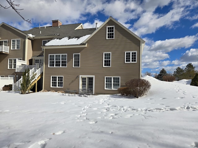 snow covered rear of property featuring stairway and a chimney