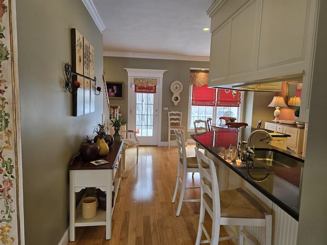 kitchen featuring light wood finished floors, baseboards, dark countertops, crown molding, and a sink