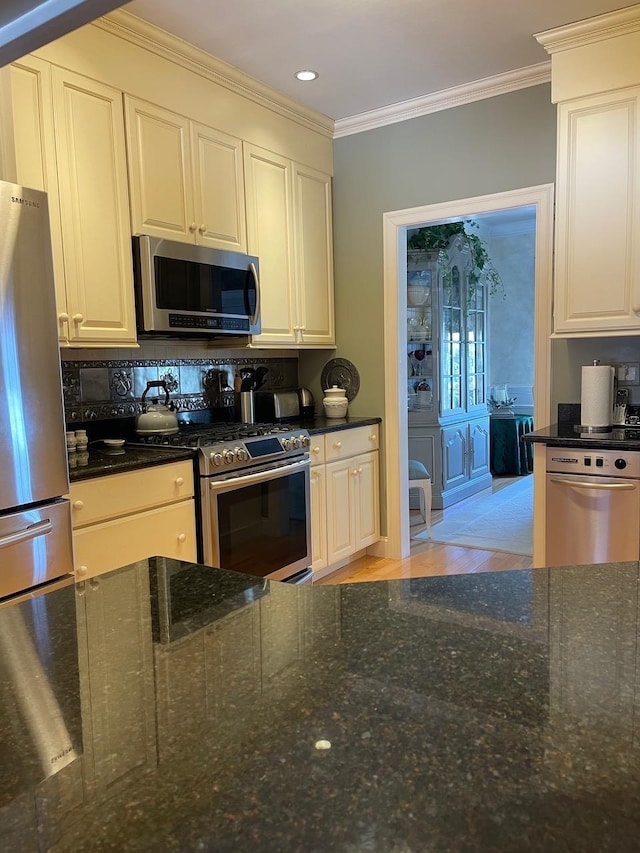 kitchen with light wood-style floors, dark stone countertops, appliances with stainless steel finishes, and crown molding