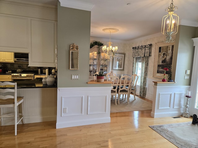 kitchen with stainless steel gas stove, light wood-style flooring, ornamental molding, a decorative wall, and a notable chandelier