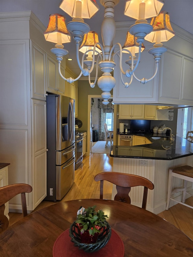 kitchen featuring stainless steel appliances, dark countertops, light wood-style flooring, an inviting chandelier, and a sink