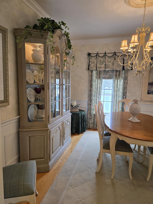 dining room with light wood-style flooring, a notable chandelier, a decorative wall, wainscoting, and crown molding