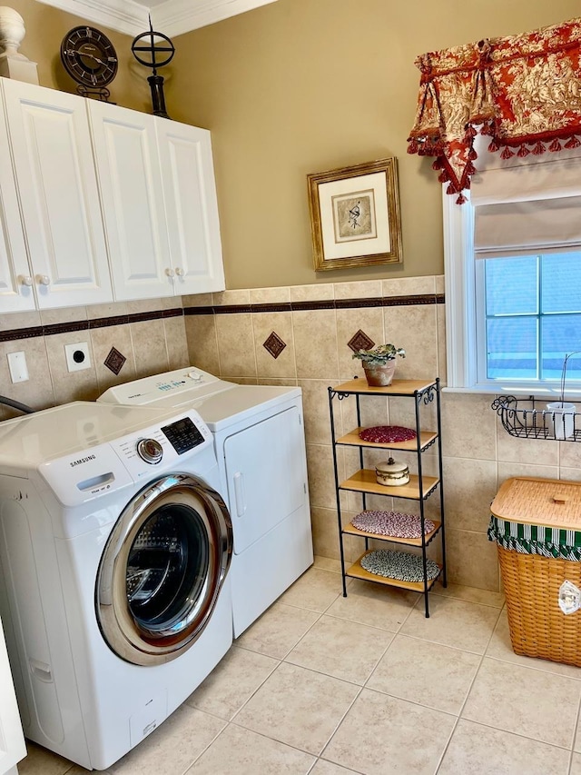 clothes washing area featuring tile walls, washing machine and clothes dryer, light tile patterned floors, cabinet space, and ornamental molding