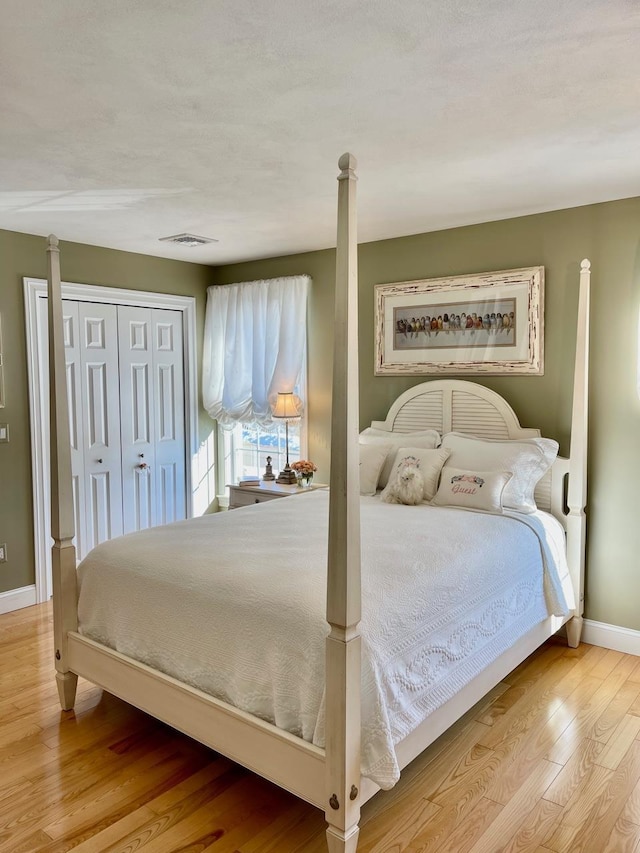 bedroom with a closet, visible vents, baseboards, and wood finished floors