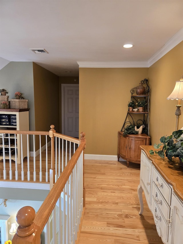 hall featuring light wood finished floors, visible vents, baseboards, ornamental molding, and an upstairs landing