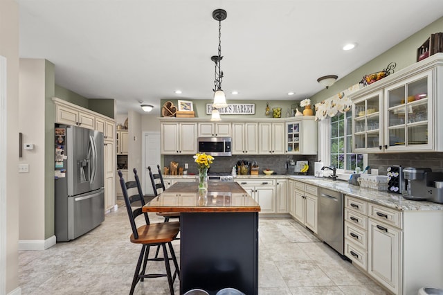 kitchen featuring appliances with stainless steel finishes, butcher block countertops, a sink, and cream cabinets