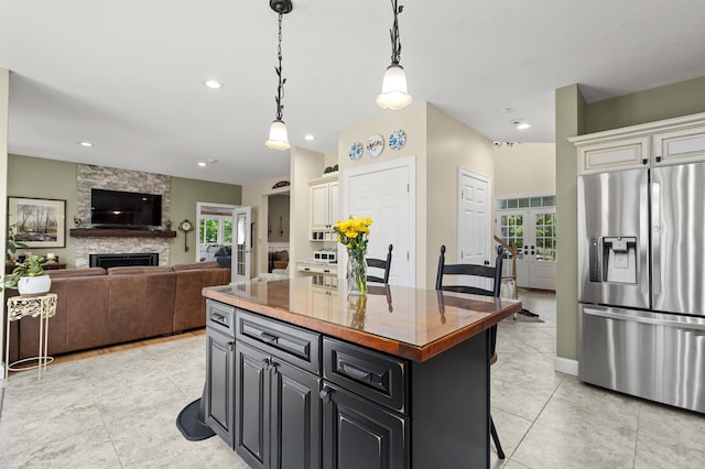 kitchen with french doors, decorative light fixtures, a fireplace, stainless steel refrigerator with ice dispenser, and a kitchen island