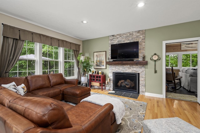 living room featuring a healthy amount of sunlight, recessed lighting, wood finished floors, and a stone fireplace