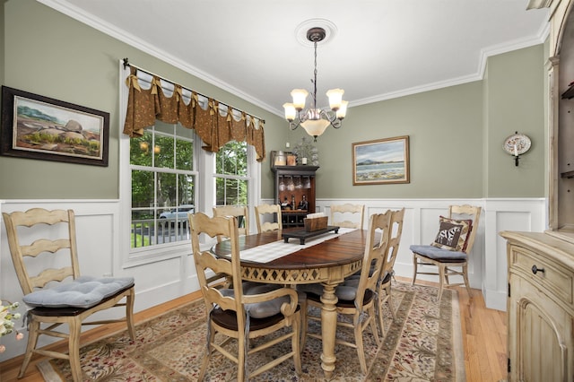 dining space with a chandelier, wainscoting, ornamental molding, and light wood-style flooring