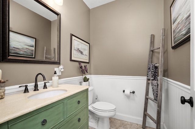 half bathroom featuring a wainscoted wall, vanity, toilet, and tile patterned floors