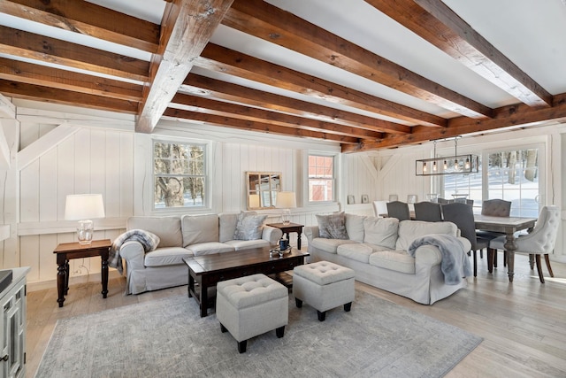 living area featuring light wood-style floors, a notable chandelier, and beamed ceiling