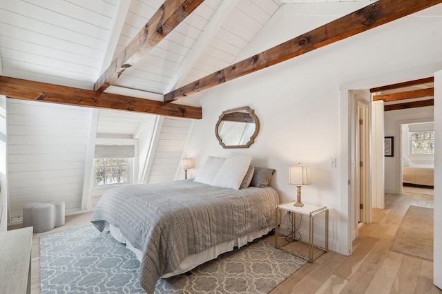 bedroom with light wood-style floors and lofted ceiling with beams