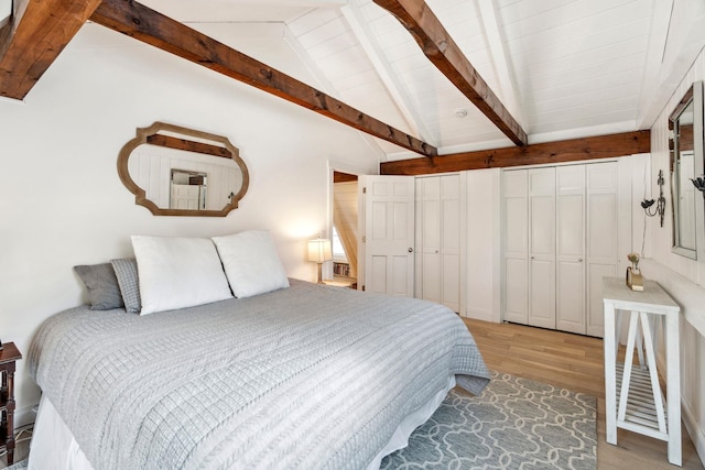 bedroom featuring lofted ceiling with beams, light wood-style flooring, and multiple closets