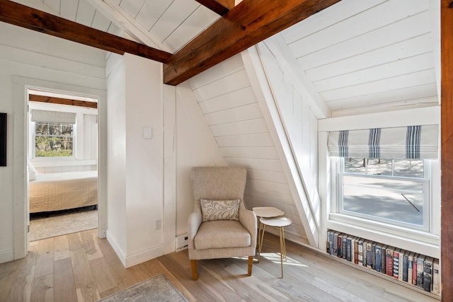 sitting room with wooden walls, baseboards, wood ceiling, vaulted ceiling with beams, and light wood-style floors