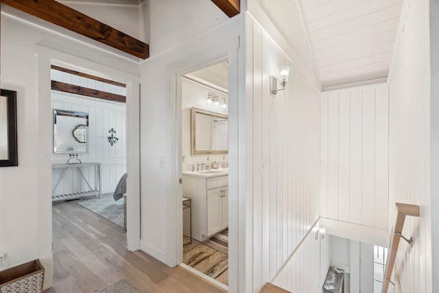 corridor with vaulted ceiling with beams, light wood-style floors, a sink, and wood walls