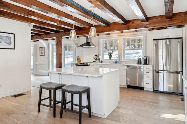 kitchen featuring stainless steel appliances, wall chimney exhaust hood, light wood-style flooring, and a center island