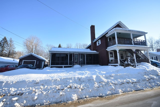 view of front of home featuring a garage, a balcony, a sunroom, a chimney, and an outdoor structure