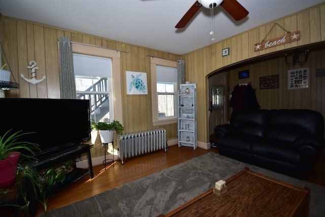 living area featuring arched walkways, baseboards, a ceiling fan, radiator heating unit, and wood finished floors