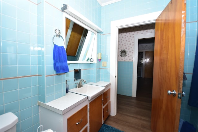 bathroom with tile walls, toilet, vanity, wood finished floors, and wallpapered walls