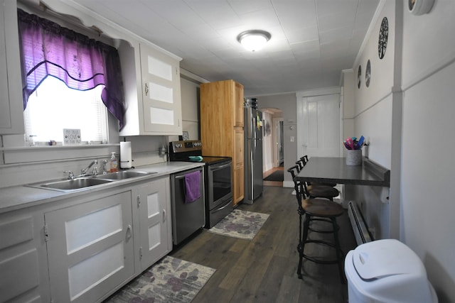 kitchen with arched walkways, dark wood-type flooring, stainless steel appliances, white cabinetry, and a sink