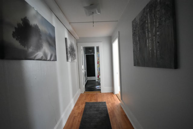 corridor with wood finished floors, attic access, and baseboards