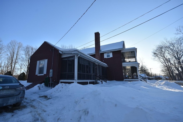 snow covered rear of property with a chimney, a sunroom, and a balcony