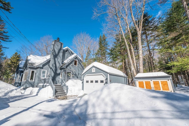 view of snow covered exterior featuring an outbuilding, a chimney, and a garage