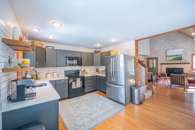 kitchen featuring light countertops, decorative backsplash, a brick fireplace, light wood-type flooring, and black appliances