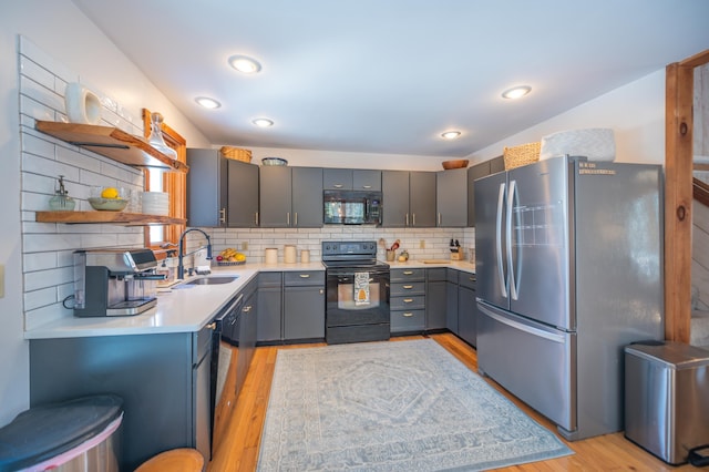 kitchen with light wood finished floors, light countertops, black appliances, open shelves, and a sink