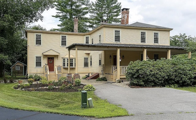 view of front facade with a front yard, covered porch, driveway, and a chimney