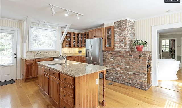 kitchen with stainless steel fridge, light stone counters, brown cabinets, light wood-style floors, and a sink